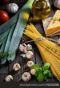 Ingredients for the preparation of pasta located on a dark wooden surface. Spaghetti, fresh vegetables, spices and olive oil for dinner. Close-up, shallow depth of field. Vegetarian lunch concept