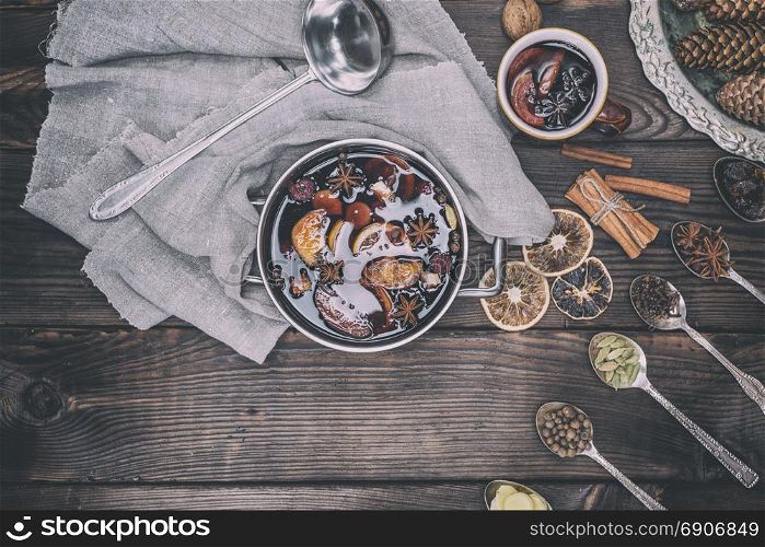 Ingredients in iron spoons for preparation of mulled wine drink and iron pot with a drink, top view, vintage toning