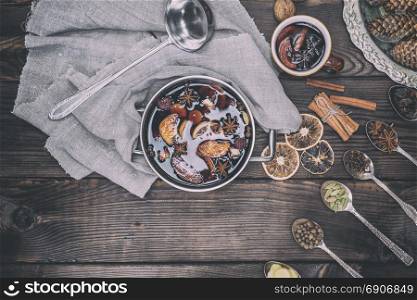 Ingredients in iron spoons for preparation of mulled wine drink and iron pot with a drink, top view, vintage toning