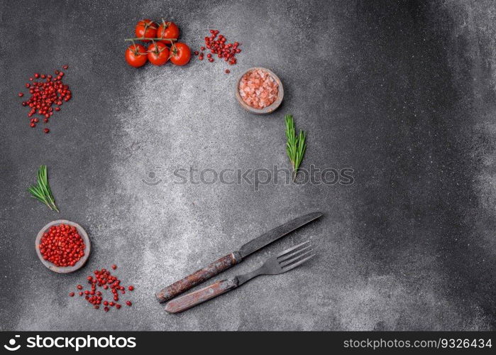 Ingredients, spices, salt, tomatoes, rosemary and cutlery knife and fork on a textured concrete background