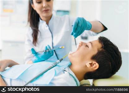 Injection of anesthesia, boy in dental chair, pediatric dentistry, children stomatology. Female dentist makes a shot. Injection of anesthesia, boy in dental chair