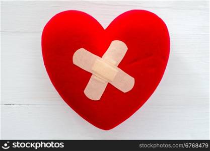 Injured heart with plaster on the white wooden surface