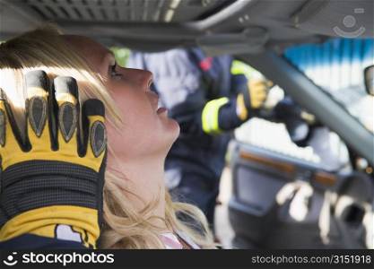 Injured woman in car with firefighter in background cutting out windshield (selective focus)