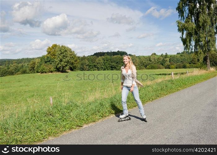 Inline skating young woman wearing jeans on sunny asphalt road