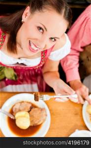 Inn or pub in Bavaria - couple in traditional Tracht drinking beer and eating roast pork with dumplings