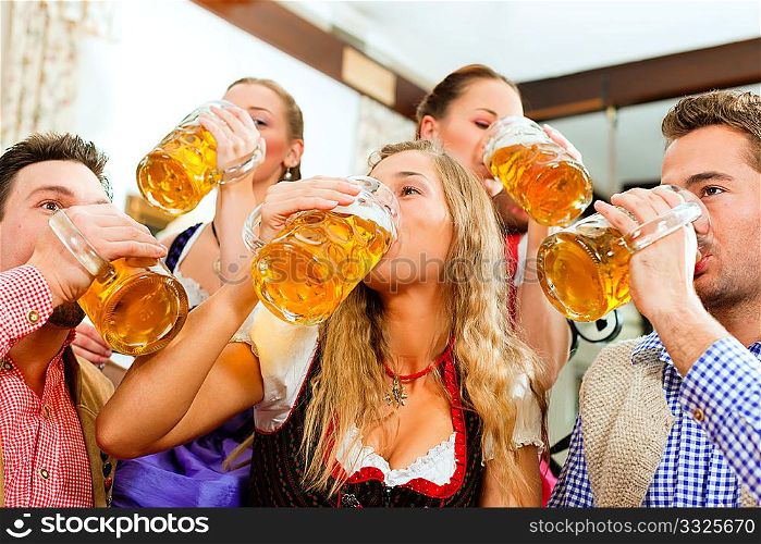 Inn or pub in Bavaria - group of five young men and women in traditional Tracht drinking beer and having a party with beer