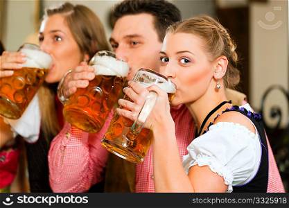 Inn or pub in Bavaria - group of three young people in traditional Tracht drinking beer