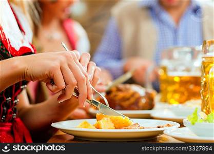 Inn or pub in Bavaria - group of young men and women in traditional Tracht drinking beer and eating roast pork with dumplings