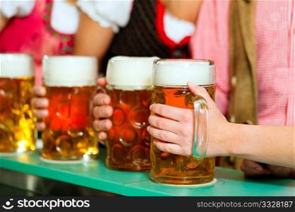 Inn or pub in Bavaria - group of young men and women in traditional Tracht having a party with beer, the steins are standing on the bar