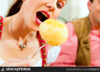 Inn or pub in Bavaria - young woman in Tracht eating dumplings she has put on her fork