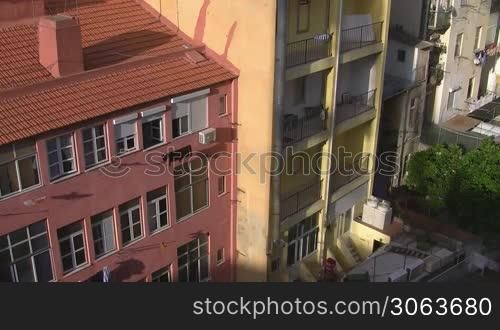 Innenhof / Hinterhof; nebeneinanderstehende hohe Mehrfamilienhaus; eines in rosa mit rotem Ziegeldach; eines in gelb mit Balkonen. Die Sonne scheint auf die Hauser.