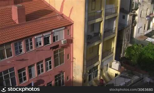 Innenhof / Hinterhof; nebeneinanderstehende hohe Mehrfamilienhaus; eines in rosa mit rotem Ziegeldach; eines in gelb mit Balkonen. Die Sonne scheint auf die Hauser.