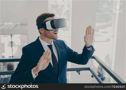 Innovative business technologies at work. Businessman in suit using virtual reality glasses in office, touching air with both hands, office worker interacting with 3d digital world. Businessman in suit using virtual reality glasses in office