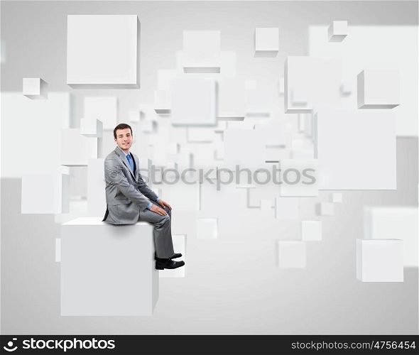 Innovative technologies. Young handsome businessman sitting on white cube