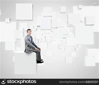 Innovative technologies. Young handsome businessman sitting on white cube