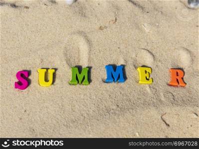 inscription summer from multi-colored wooden letters on sand, top view