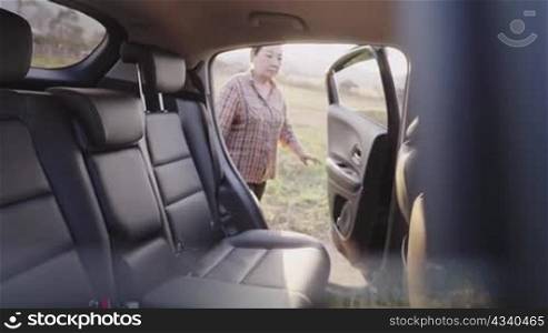 Inside car shooting: Asian black hair senior stepping in a family car, elderly gets herself ready by sitting on a backseat and wait for others coming, physical aging affect movements