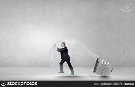 Inside light bulb. Businessman inside light bulb trying to get out