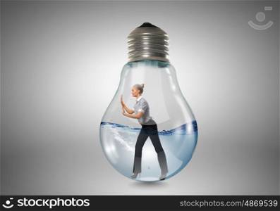 Inside light bulb. Businesswoman inside light bulb trying to get out