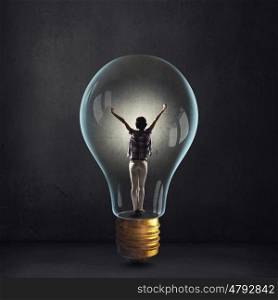 Inside of bright idea. Cheerful girl inside of glass light bulb on dark background