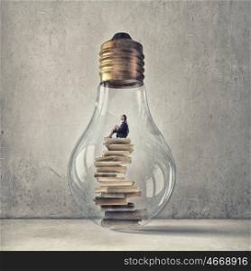 Inside of idea bulb. Young woman sitting om books stack inside of glass light bulb
