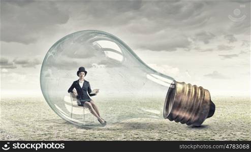 Inside of idea bulb. Young woman with tablet pc sitting inside of glass light bulb
