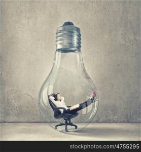 Inside of idea. Relaxed businesswoman sitting inside of glass light bulb