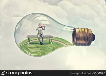 Inside of idea. Young businessman inside of glass light bulb playing violin
