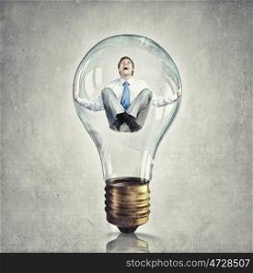 Inside of idea. Young businessman trapped inside of light bulb and calling for help