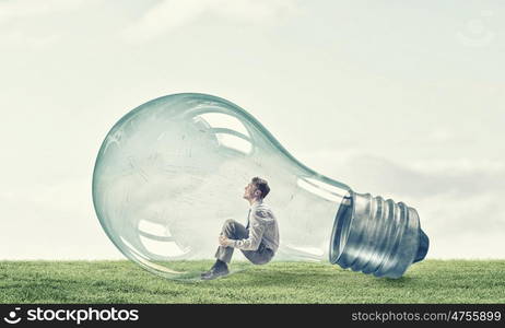 Inside of idea. Young thoughtful businessman trapped inside of light bulb