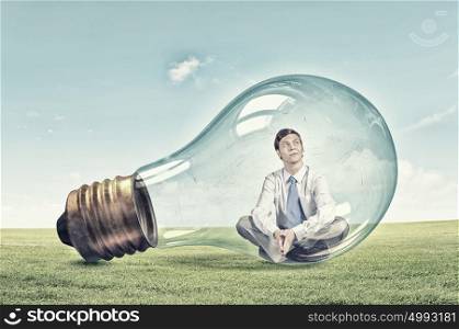 Inside of idea. Young thoughtful businessman trapped inside of light bulb