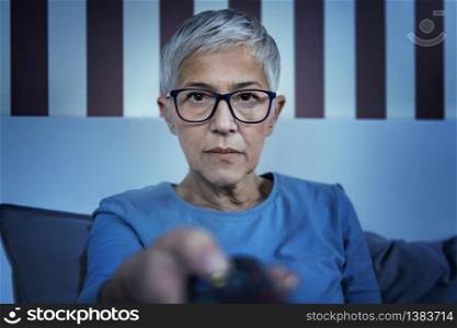 Insomnia. Mature woman sitting on bed, watching television late at night. Insomnia. Mature Woman Watching Television Late at Night