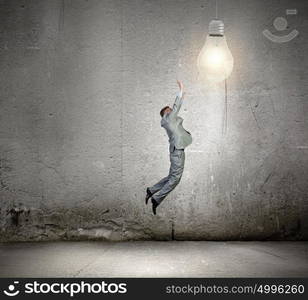 Inspiration and idea. Image of young businessman jumping and catching light bulb