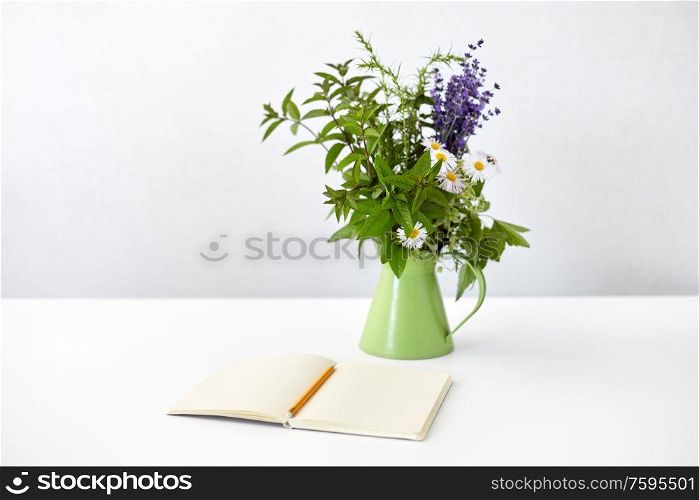 inspiration concept - notebook or sketchbook with pencil and bunch of flowers in green jug on white table. notebook with pencil and bunch of flowers in jug