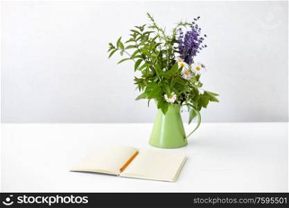 inspiration concept - notebook or sketchbook with pencil and bunch of flowers in green jug on white table. notebook with pencil and bunch of flowers in jug