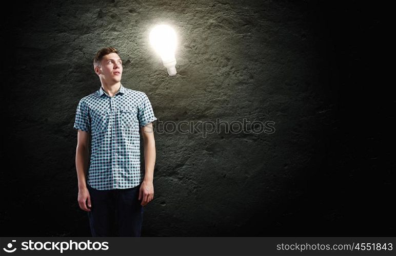 Inspiration concept. Young man and electrical bulb against dark background