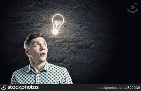 Inspiration concept. Young man and electrical bulb against dark background