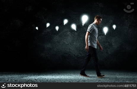 Inspiration concept. Young man and electrical bulb against dark background