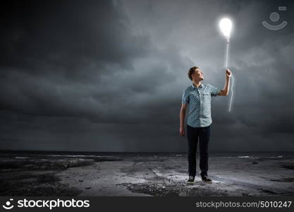 Inspiration concept. Young man and electrical bulb against dark background