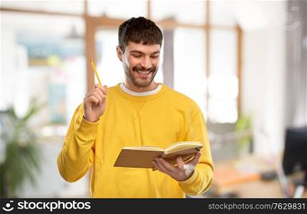 inspiration, idea and people concept - smiling young man in yellow sweatshirt with diary and pencil over office background. happy man in yellow sweater with diary and pencil