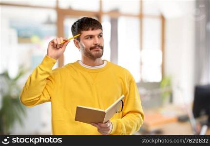 inspiration, idea and people concept - thinking young man in yellow sweatshirt with diary and pencil over office background. thinking man with diary and pencil over office