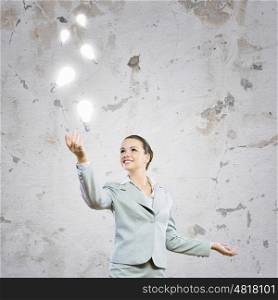 Inspiration. Image of attractive smiling businesswoman holding light bulbs on hand