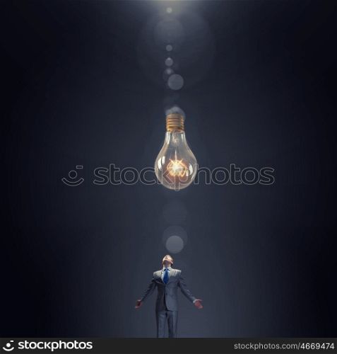 Inspirational idea. Young businessman looking up at huge hanging lightbulb