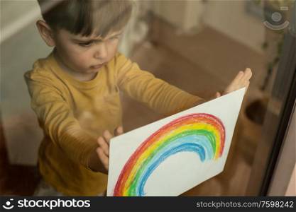 Inspirational little kid holding a drawing of a rainbow through the window