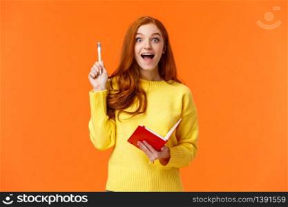 Inspired and dreamy, smart redhead female student got excellent idea for her book, write in notebook plans and to-do list, raising pen in eureka gesture and smiling astonished, orange background.. Inspired and dreamy, smart redhead female student got excellent idea for her book, write in notebook plans and to-do list, raising pen in eureka gesture and smiling astonished, orange background