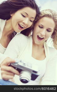 Instagram filter style photograph of two young women girls, one Asian Chinese, one blond, laughing looking at photographs on digital camera