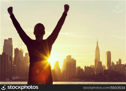 Instagram style filter silhouette of a successful woman or girl arms raised celebrating at sunrise or sunset in front of the New York City Skyline