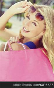 Instagram style photograph of beautiful, happy and fashionable young blond woman with heart shaped sunglasses and colorful shopping bags over her shoulder.