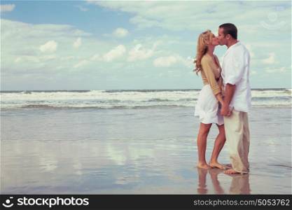 Instagram style photograph of romantic young man and woman couple holding hands and kissing on a beach