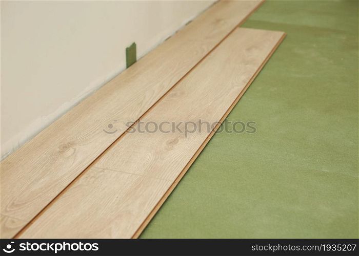 Installing wooden laminate or parquet floor in room over green base. assembling panels quickly and easily - affordable flooring. laying laminate flooring at home.. Installing wooden laminate or parquet floor in room over green base. assembling panels quickly and easily - affordable flooring. laying laminate flooring at home
